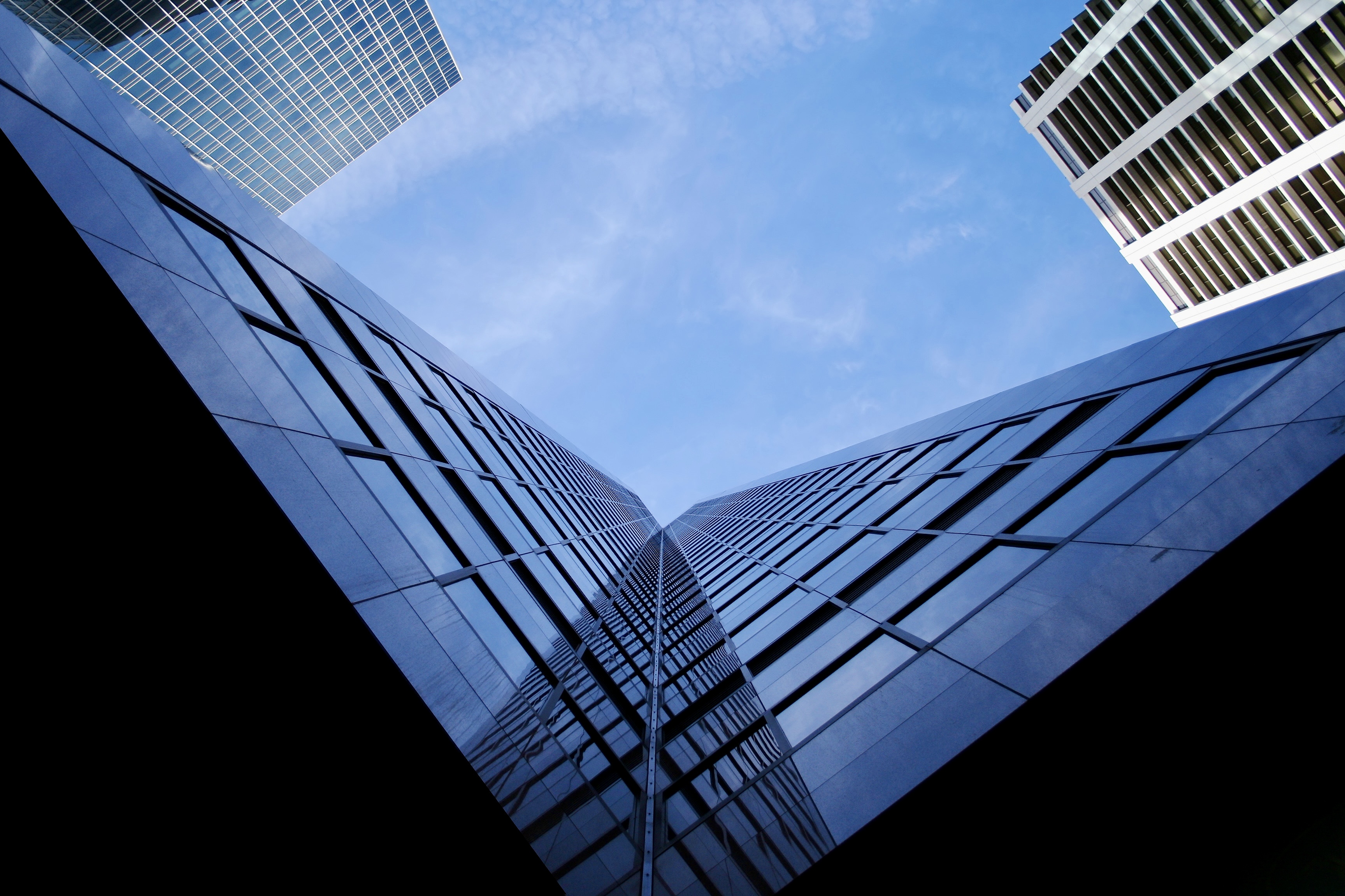 Low angle of a tall downtown building. Looking up at an in shadow skyscraper. City architecture. Windows reflecting blue sky.